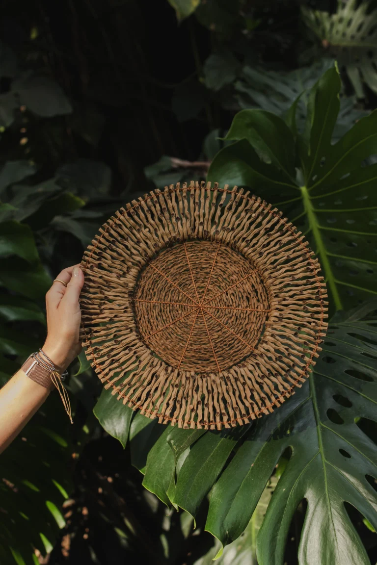 Mano sosteniendo salvamanteles artesanal de fibra con fondo de monstera – Areito Gallery