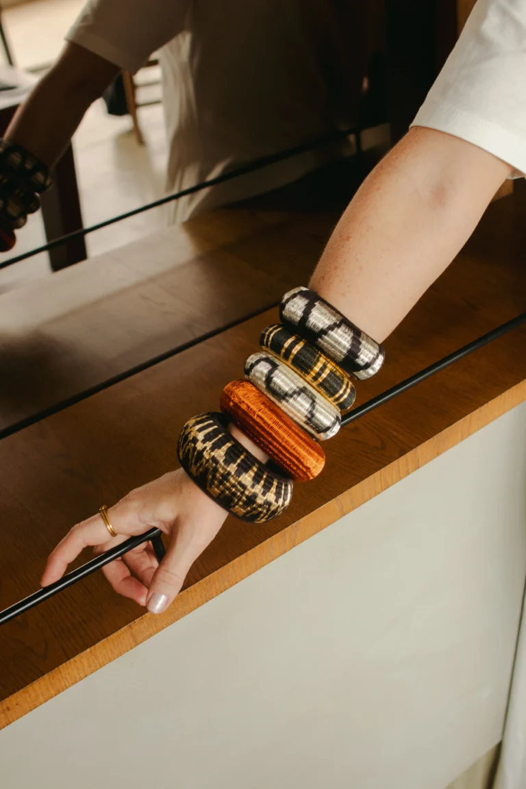 Muñeca con pulseras artesanales tejidas apiladas en distintos patrones sobre mesa – Areito Gallery